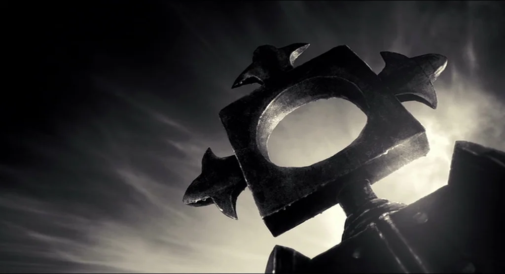 Sin City (2005) movie still: closeup — A metallic ornamental structure with a central ring stands against a dark cloudy sky. Sunlight flares from…