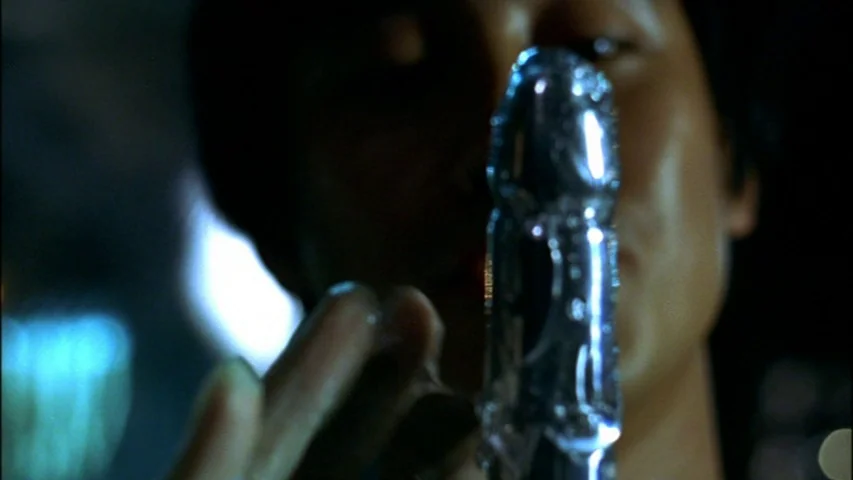 Save The Green Planet! (2003) movie still: closeup — A dark environment provides the backdrop for a close-up examination of a glass object. An…