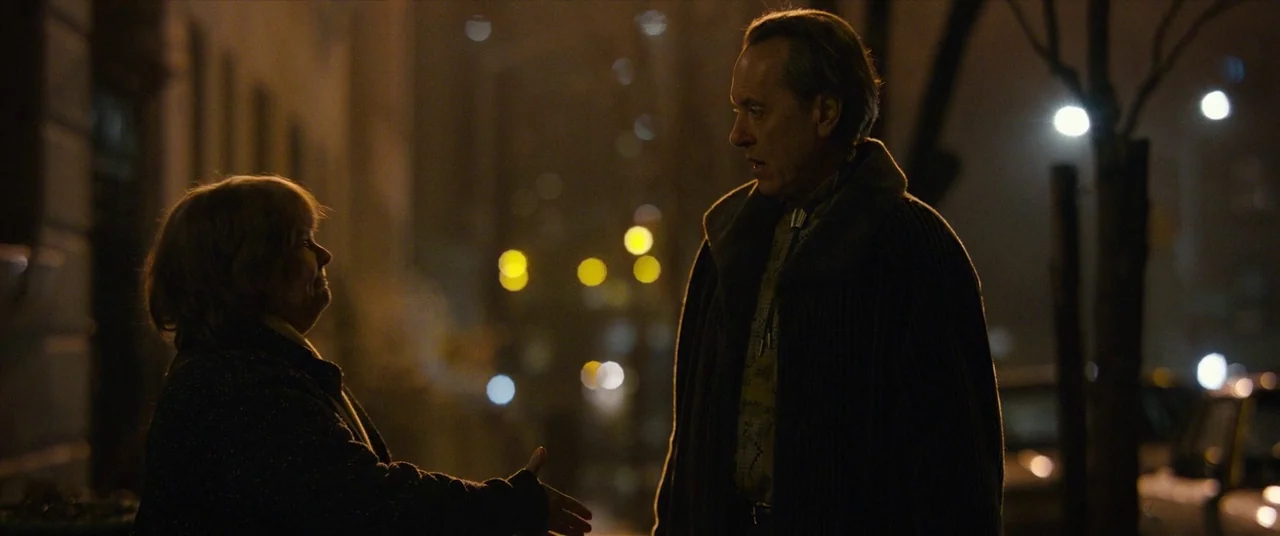 Can You Ever Forgive Me? (2018) movie still: medium — An urban sidewalk at night is illuminated by blurry, out-of-focus street lighting. A woman…