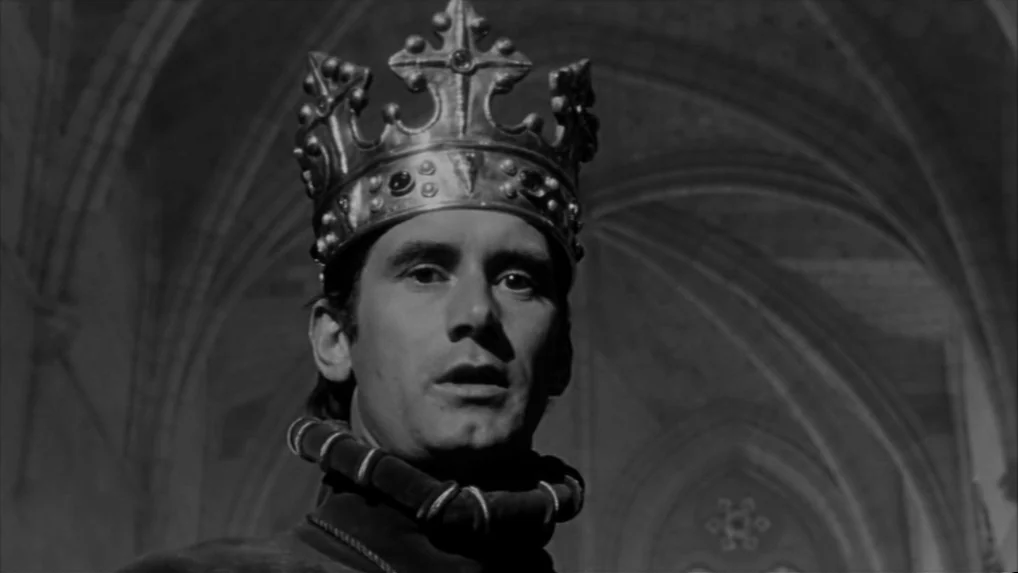 Falstaff (Chimes at Midnight) (1965) movie still: closeup — A man wearing a metal crown stands in a dark stone cathedral nave. He stares forward…