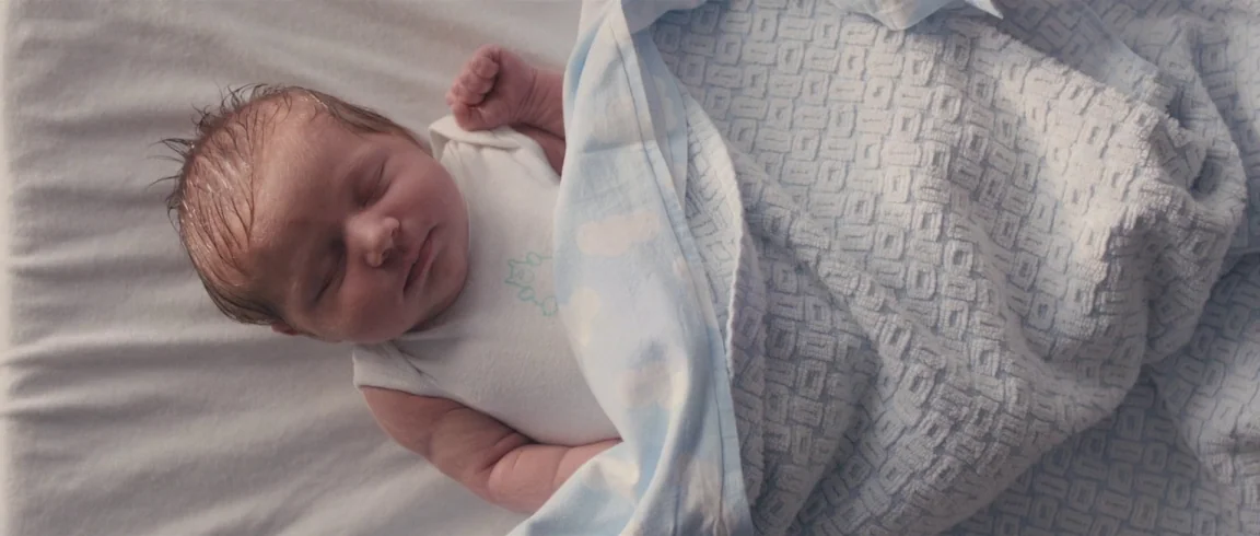 Broken Circle Breakdown (2012) movie still: closeup — A newborn baby lies on a white mattress. The infant is covered by a textured blue blanket.