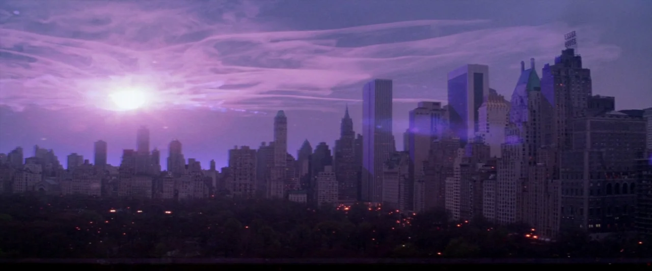 Ghostbusters 2 (1989) movie still: establishing — A wide view of the Manhattan skyline appears under a deep violet sunset sky. Many tall apartment…