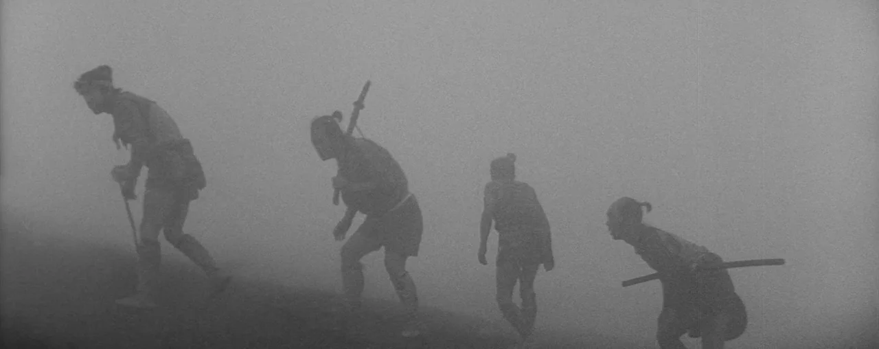 The Hidden Fortress (1958) movie still: wide — Four men move in profile through a thick, obscuring fog on a hillside. The figures carry swords and…