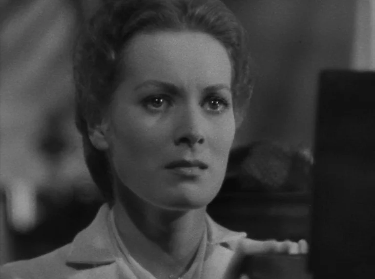 Rio Grande (1950) movie still: closeup — A woman stares forward with a fixed expression in a dimly lit interior. Her face is illuminated against the…
