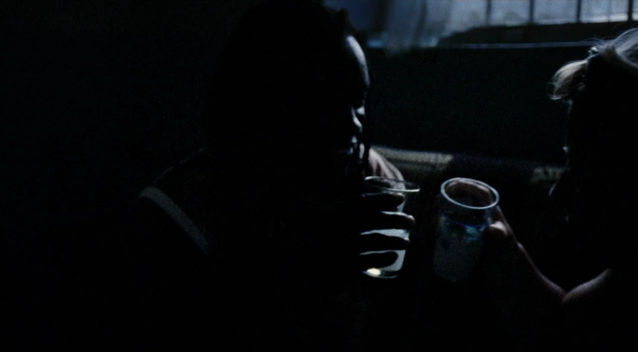 Paradise: Love (2012) movie still: medium — A dimly lit, dark interior space features two people sitting near each other. They hold drinking glasses…