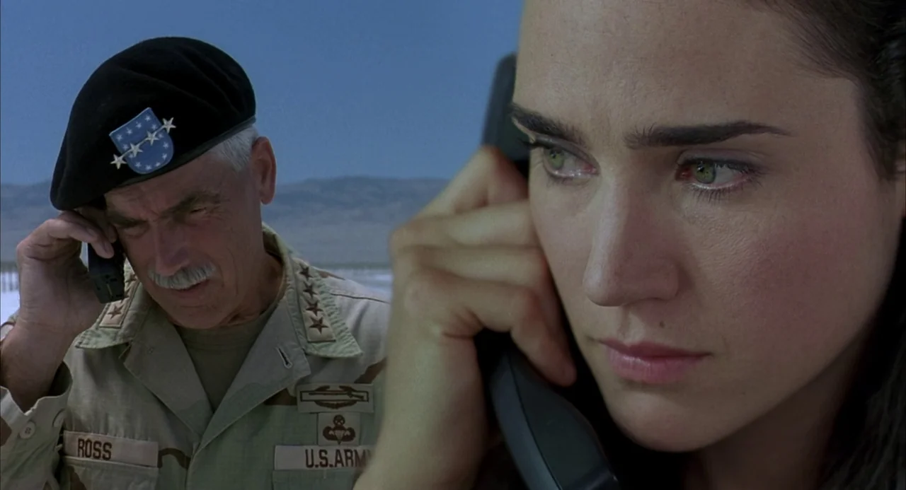 Hulk (2003) movie still: closeup — A split composition shows a woman in the foreground and a military general behind. The desert landscape stretches…