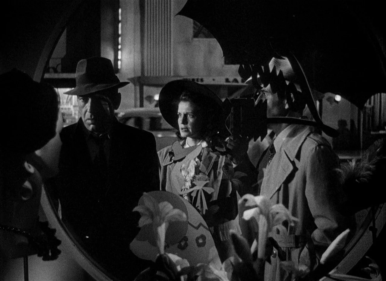 Dead Reckoning (1946) movie still: medium — A dark night scene outside a city storefront with decorative paper displays visible. Three individuals…