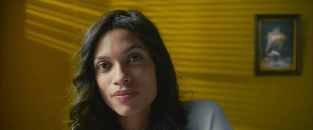 Trance (2013) movie still: closeup — A yellow-walled space features horizontal light streaks from window blinds on the surface. A woman looks…