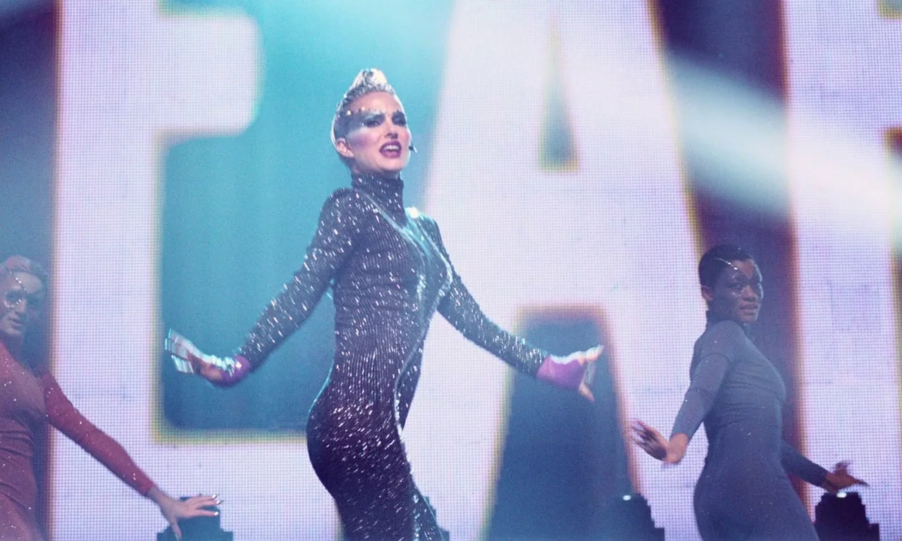 Vox Lux (2018) movie still: medium — A performer stands center stage in front of a giant illuminated letter display. She performs a choreographed…