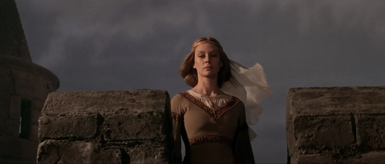 Macbeth (1971) movie still: medium — A stone castle battlement stands against a dark, cloudy sky. A woman wearing a medieval dress stands between…