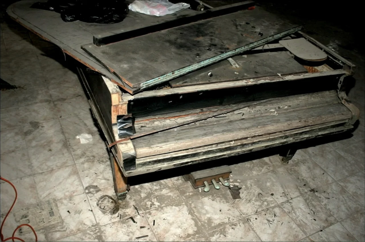 Dark Light: The Art of Blind Photographers (2009) movie still: medium — A broken, wooden grand piano sits on a tiled floor in a dark room. The lid…