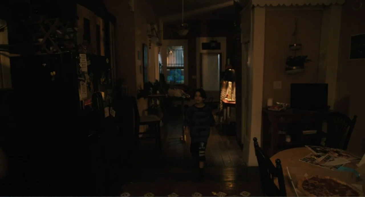 Mona Lisa and the Blood Moon (2022) movie still: medium — A dimly lit indoor hallway connects two rooms of a residential house at night. A young…