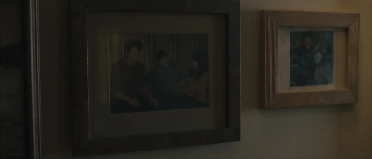 All Fun and Games (2023) movie still: closeup — A plain interior wall features two rectangular picture frames mounted horizontally side by side.…