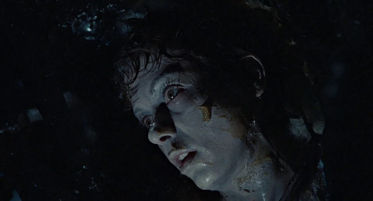 Aliens (1986) movie still: closeup — A dark, cramped interior setting with wet, cavernous textures visible in the background. A woman with pale skin…