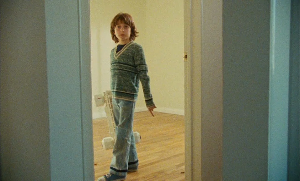 Documenteur (1981) movie still: fullbody — An empty room with light hardwood floors and plain beige walls seen through a doorway. A young boy…