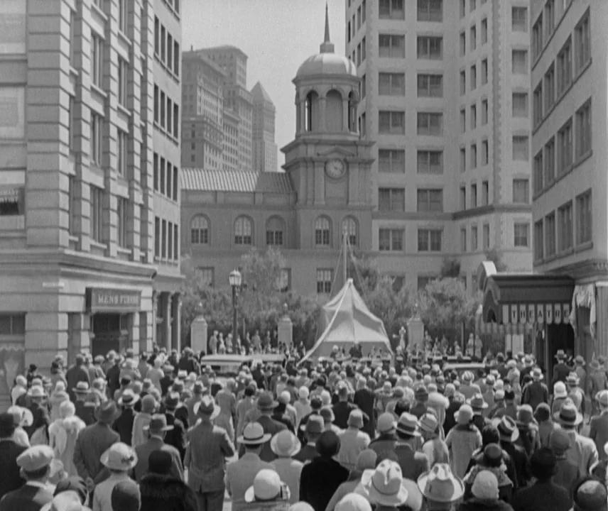 City Lights (1931) movie still: establishing — A dense crowd of people in 1940s-style clothing gathers in a city plaza square. In the distance, a…