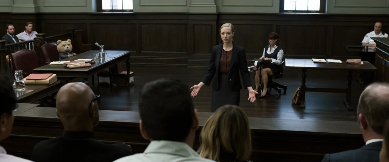 Ted 2 (2015) movie still: medium — A wood-paneled courtroom features jury benches in the foreground and a stenographer seated behind. A woman in a…