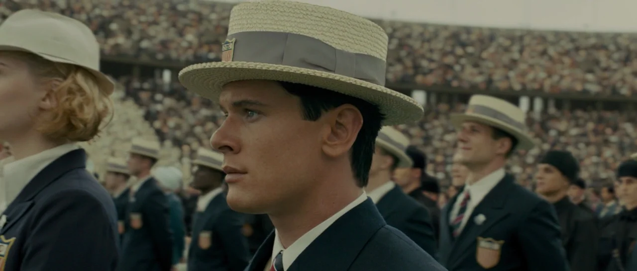 Unbroken (2014) movie still: medium — A large outdoor stadium filled with spectators under an overcast sky. Numerous people in matching navy blue…
