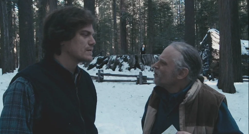 My Son, My Son, What Have Ye Done? (2009) movie still: medium — A snowy wooded area features large tree trunks and a large old tree stump. Two men…
