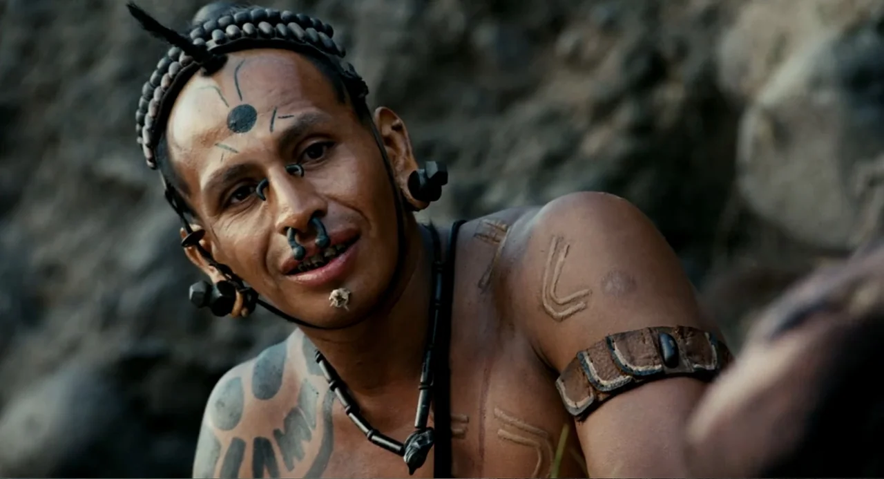Apocalypto (2006) movie still: medium — A rocky exterior environment with a blurred stone background behind the subject. A indigenous man with body…