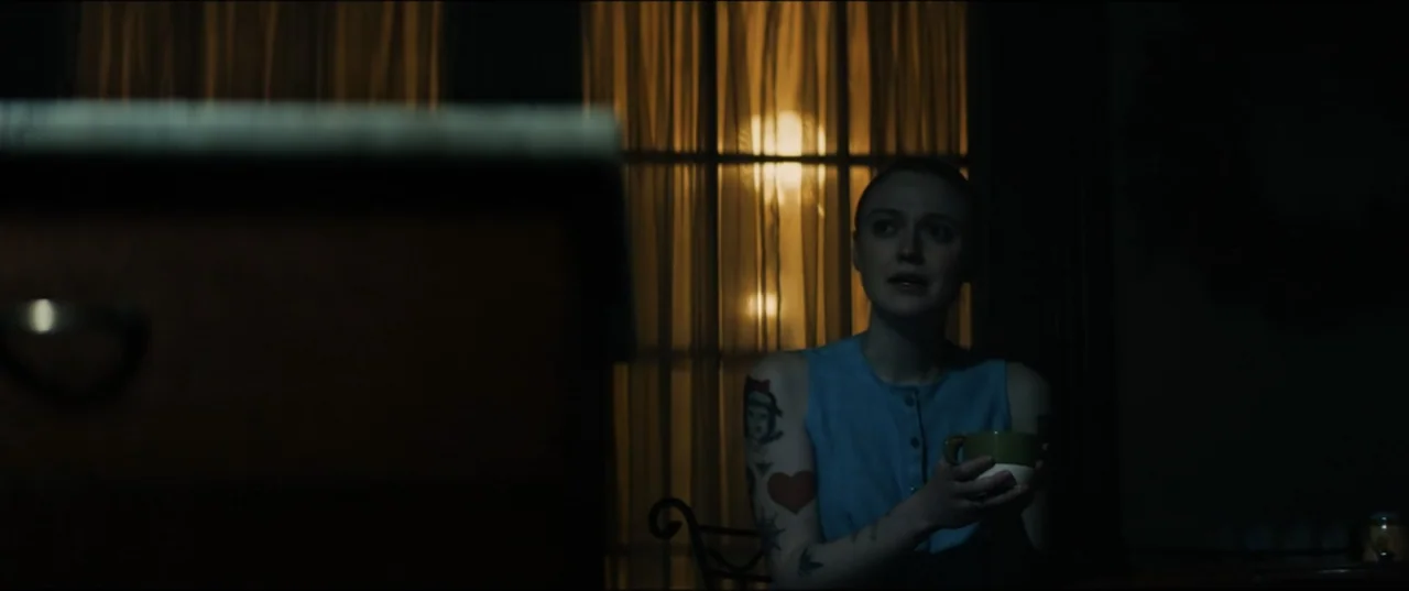Vicious (2025) movie still: medium — A dark indoor space features a window covered by thin curtains at night. A young woman sits alone holding a mug…