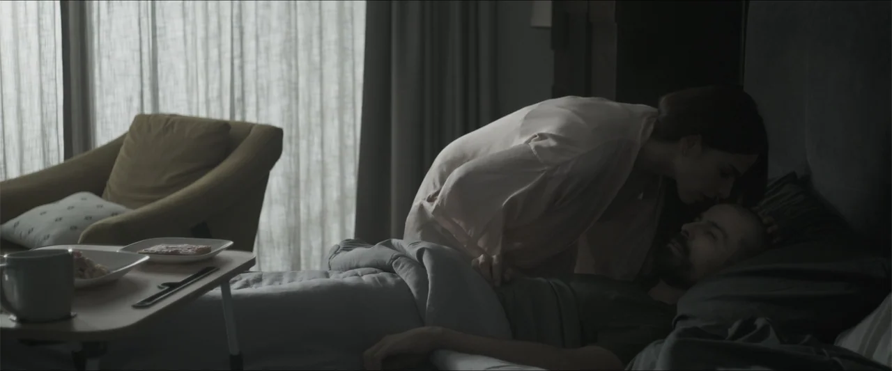 Los habitantes (2023) movie still: medium — A modern bedroom with a large window covered by light translucent curtains. A woman leans over a man…