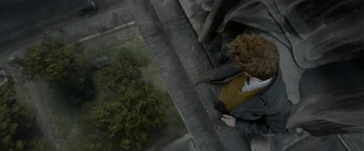Fantastic Beasts: The Crimes of Grindelwald (2018) movie still: medium — A man stands on the narrow stone ledge of a tall building exterior. He…