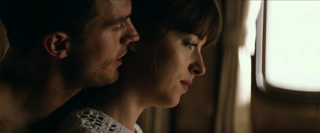 Fifty Shades Freed (2018) movie still: closeup — An airplane cabin interior features a bright window on the right side. A man leans toward a woman…