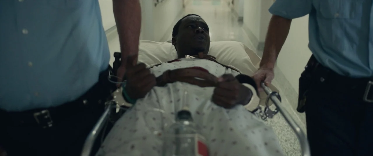 Judas and the Black Messiah (2021) movie still: medium — A long, brightly lit hospital corridor with polished floors and white walls. A man in a…