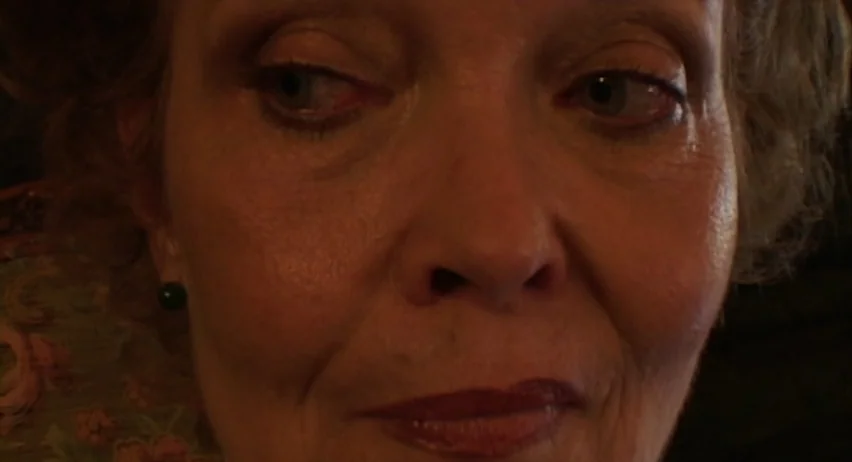 Inland Empire (2006) movie still: closeup — A dark indoor space provides the setting for a portrait of an elderly woman. She remains centered in the…