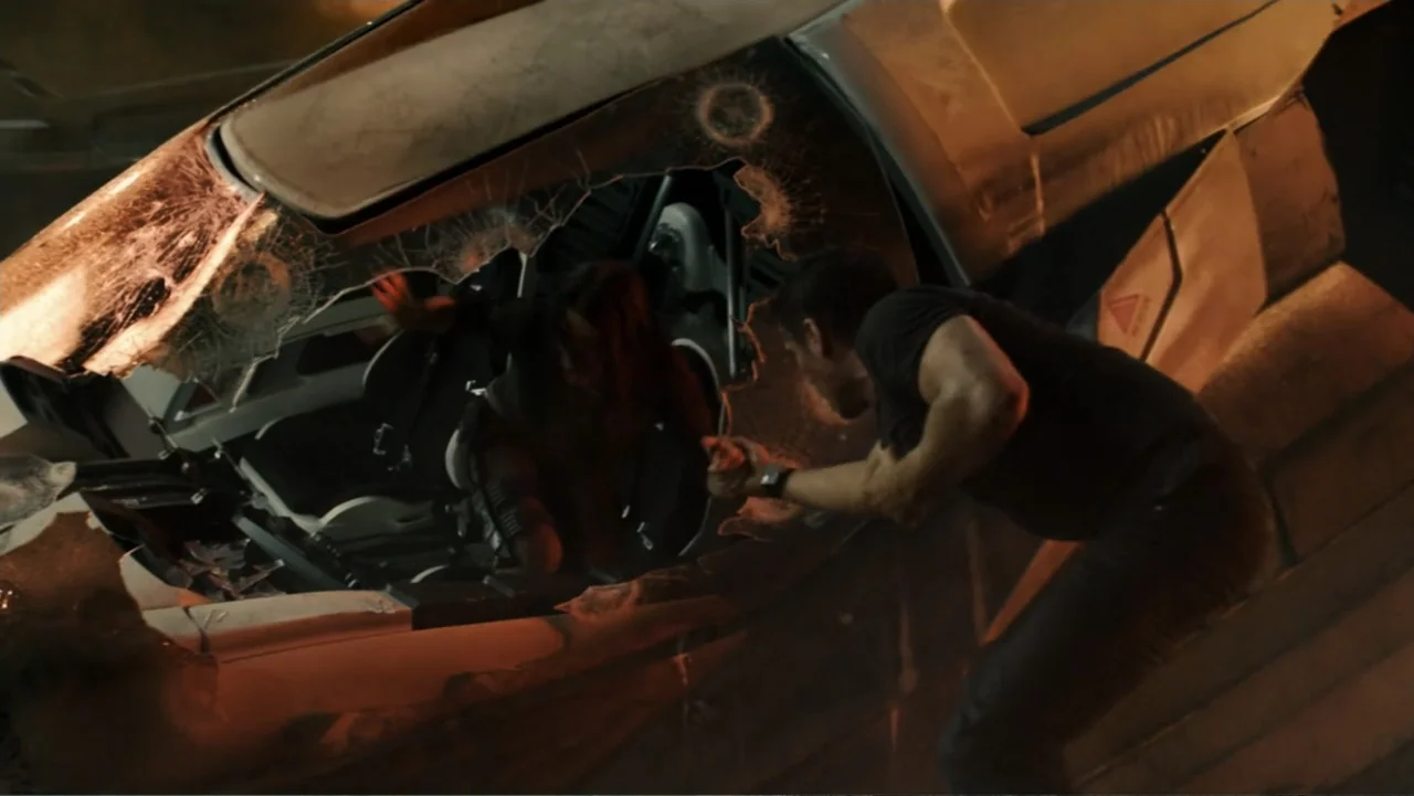 Total Recall (2012) movie still: medium — A damaged futuristic vehicle rests in an dark outdoor space at night. A man attempts to pull a woman from…