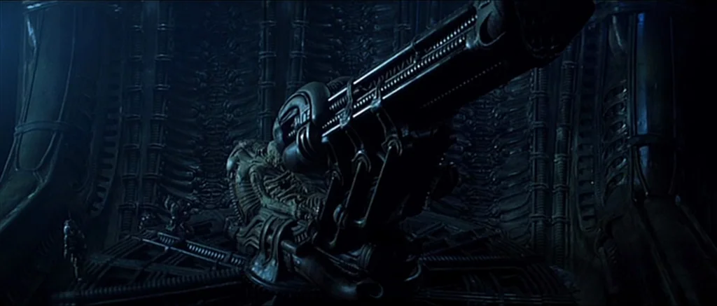 Alien (1979) movie still: wide — A dark, intricate alien chamber features bio-mechanical wall textures and central technical apparatus. A large…