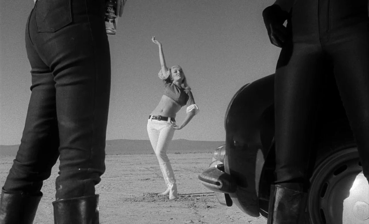 Faster, Pussycat! Kill! Kill! (1965) movie still: medium — A vast, dry desert expanse under a clear sky. A woman stands between two figures as she…
