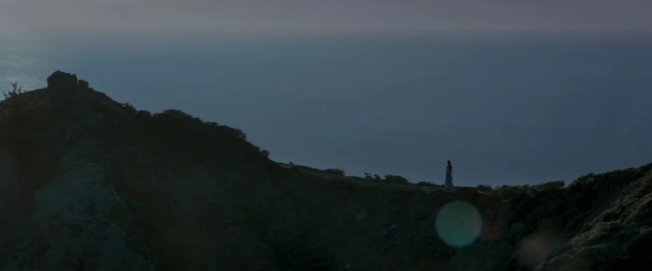 Memoirs of a Geisha (2005) movie still: wide — A rugged coastal ridge overlooks a vast, calm sea under an overcast grey sky. A lone woman in a long…