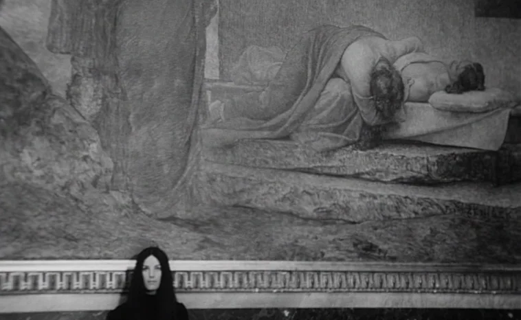 The Cremator (1969) movie still: medium — A woman stands before a large monochrome painting displayed on an interior gallery wall. The painting…