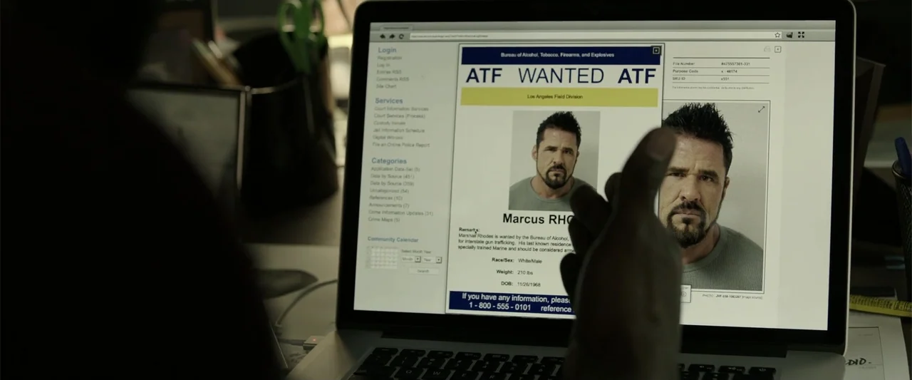 Den of Thieves (2018) movie still: medium — A dimly lit office features a laptop screen displaying an ATF wanted poster. A person's blurred…
