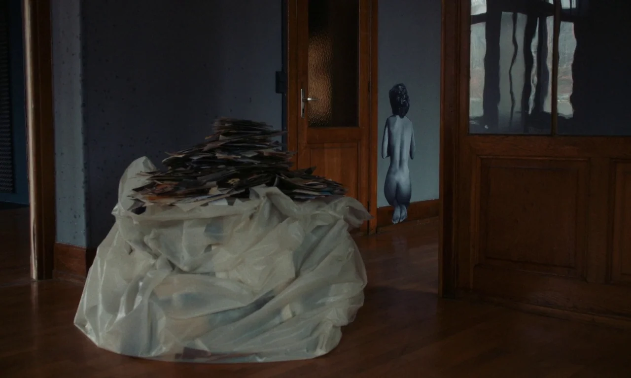 Little Girl Blue (2023) movie still: medium — A quiet residential hallway features a large plastic bag filled with stacked paper piles. A figure…
