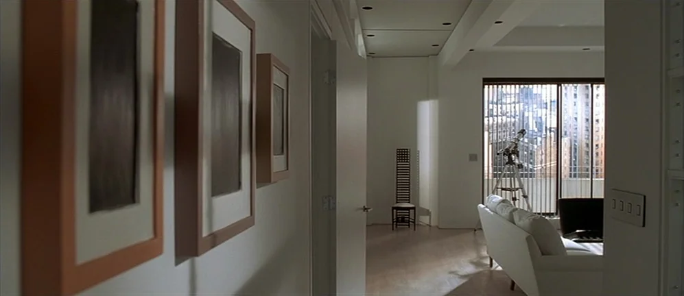 American Psycho (2000) movie still: wide — A bright, minimalist apartment hallway leads into a living room with a large window. A telescope stands…