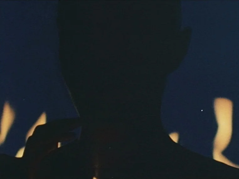 Salome (1972) movie still: closeup — A dark night setting shows the silhouette of a person standing before flames. The subject is partially visible…