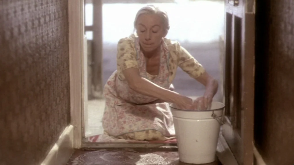 Distant Voices, Still Lives (1988) movie still: medium — A woman kneels on the floor by an open doorway, scrubbing a cloth. The setting is a modest…