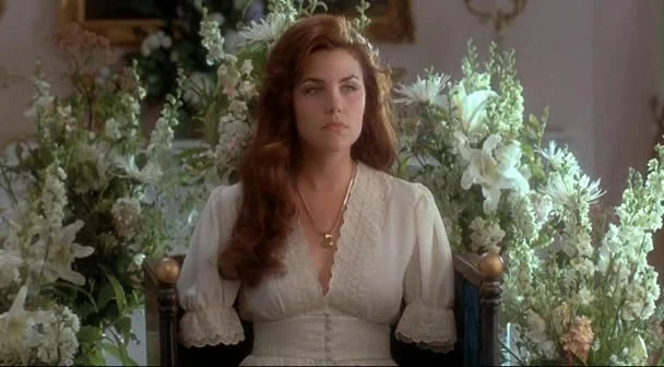 Boxing Helena (1993) movie still: medium — A woman sits in a chair surrounded by dense arrangements of white funeral flowers. The room features a…