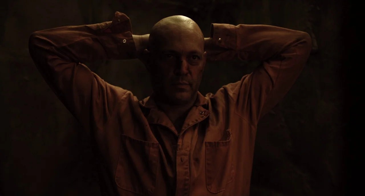 Brawl in Cell Block 99 (2017) movie still: medium — A dark, dimly lit environment with textured walls suggesting a confined space. A man in an…