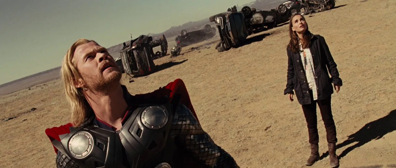 Thor (2011) movie still: medium — A vast arid landscape features multiple overturned vehicles scattered across the sandy ground. A man in metal…