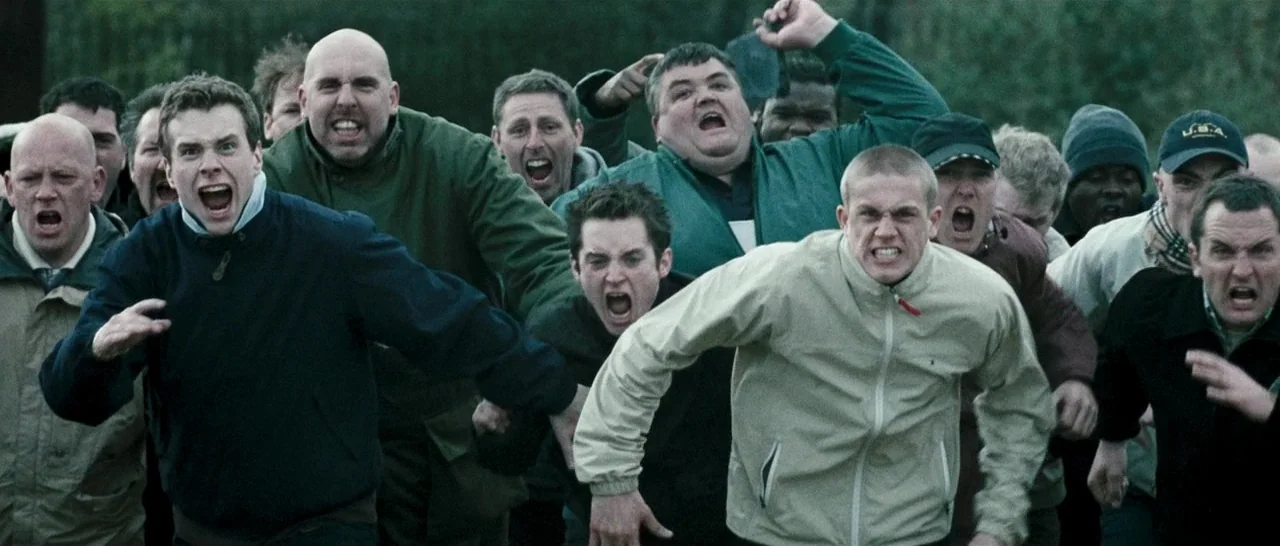 Green Street (2005) movie still: medium — A crowd of men in casual jackets runs forward through an outdoor area. The men are shouting with intense,…