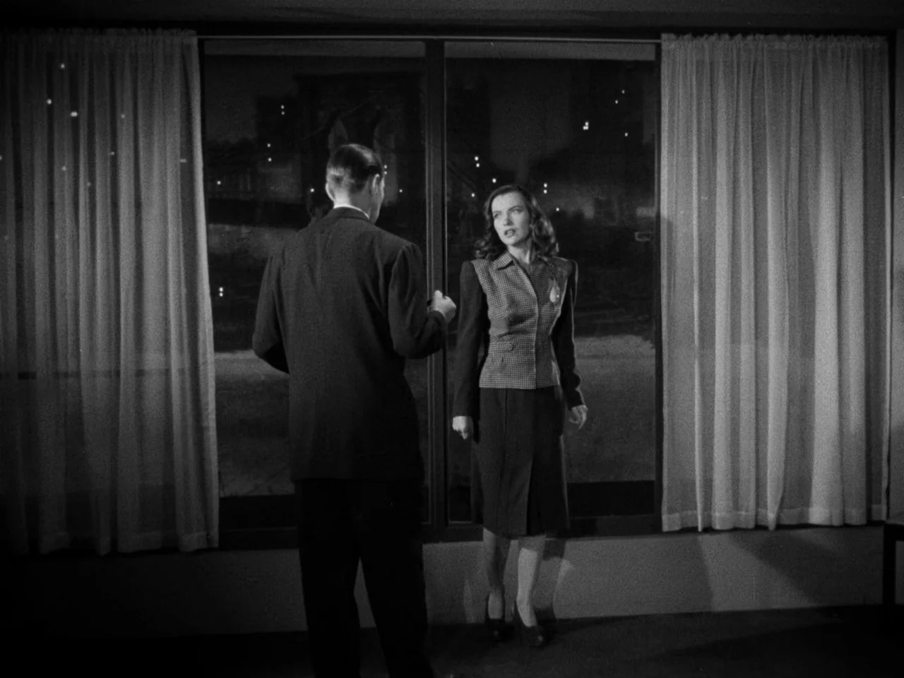 Phantom Lady (1944) movie still: fullbody — A stark room features a large window overlooking a dark exterior at night. A man stands with his back to…