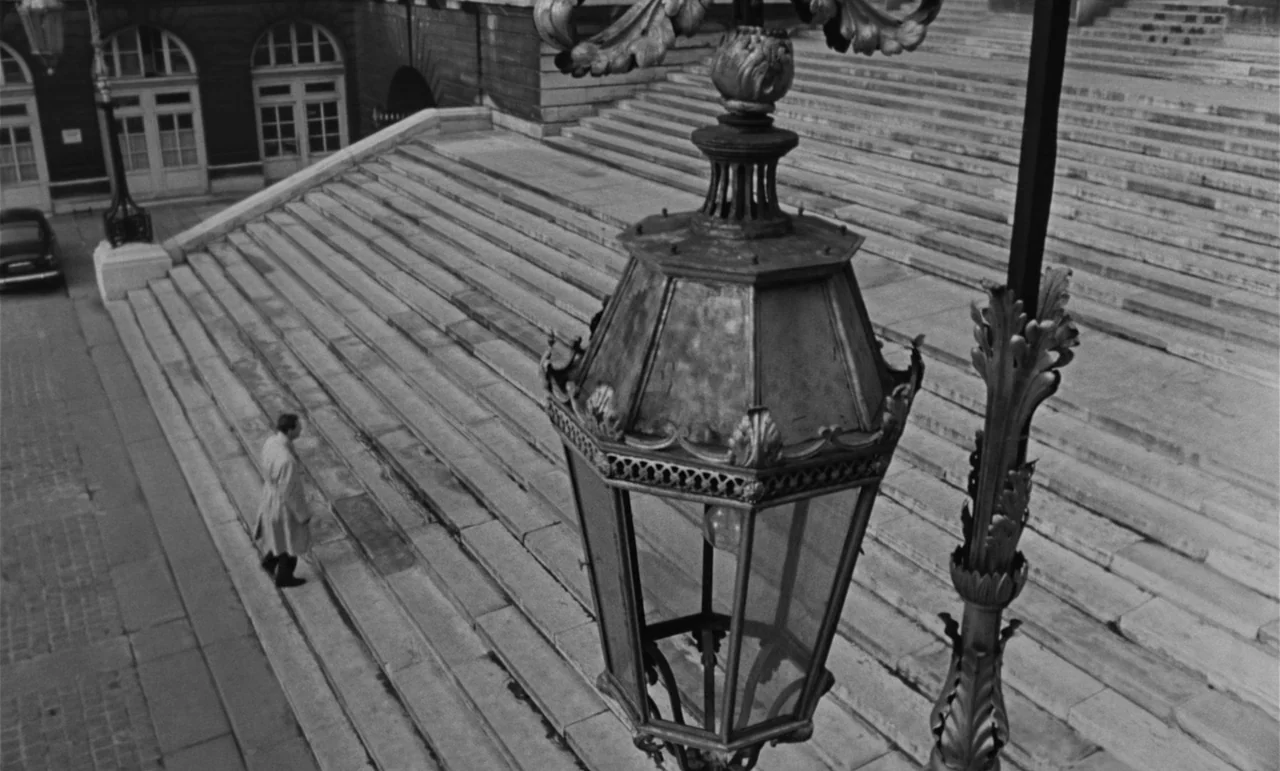 Witness In The City (1959) movie still: wide — A wide set of stone stairs descends toward a building with arched doorways. A man in a light coat…
