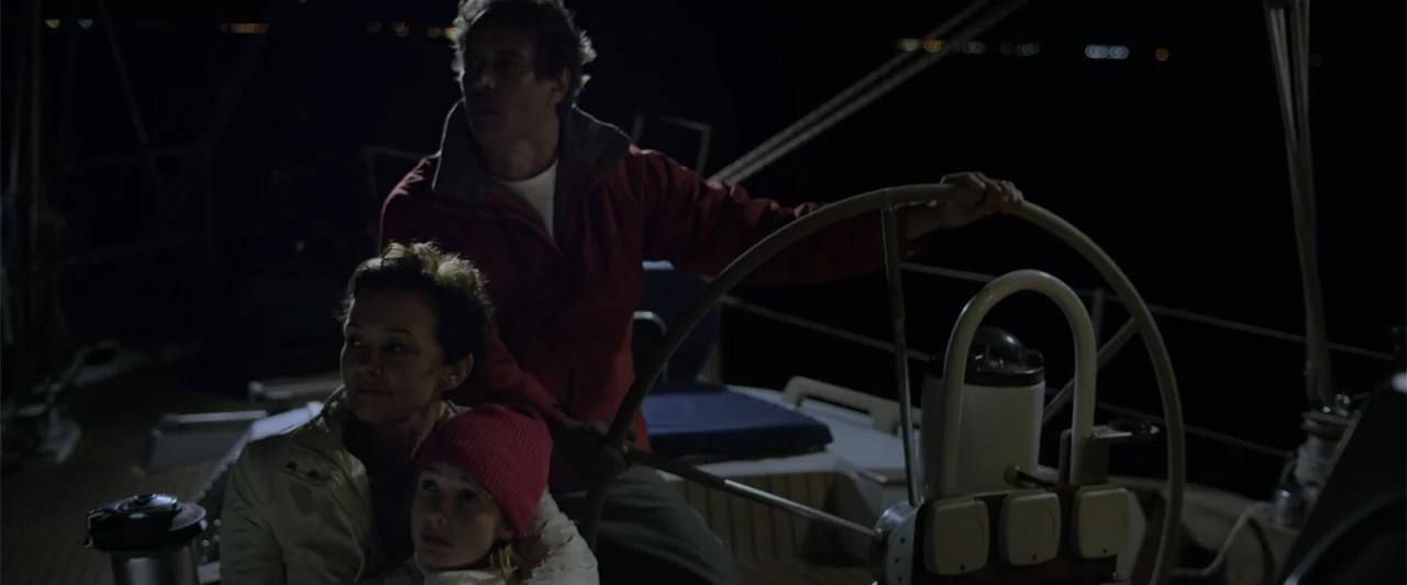 Dirty Little Secret (1998) movie still: medium — The deck of a modern sailboat at night during calm water conditions. A man operates the steering…