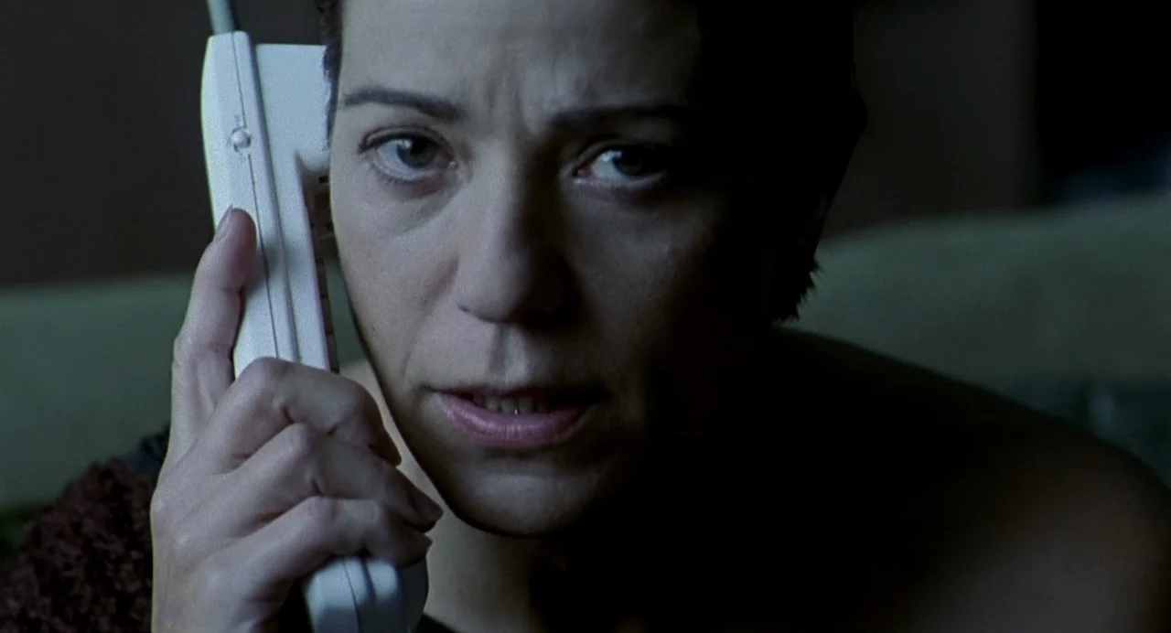 The Nameless (1999) movie still: closeup — A dark, dimly lit indoor space with low-key illumination. A woman holds a white cordless telephone…