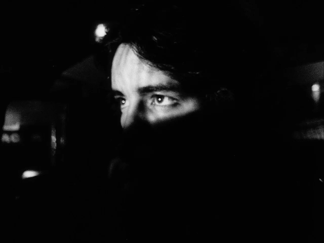 Mala Noche (1986) movie still: closeup — A man's face emerges from total darkness in a dimly lit interior space. His eyes and brow are illuminated…