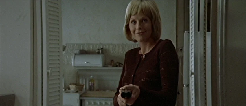 Images (1972) movie still: medium — A woman stands in a doorway framed by white louvered doors. She holds a shotgun pointed directly toward the…